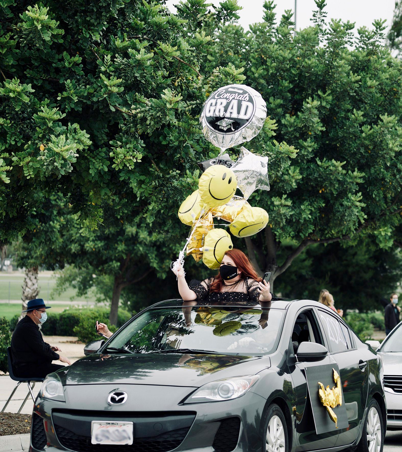 A La Sierra University graduate holds balloons out of a car's sunroof during the "Drive-Through Celebration."