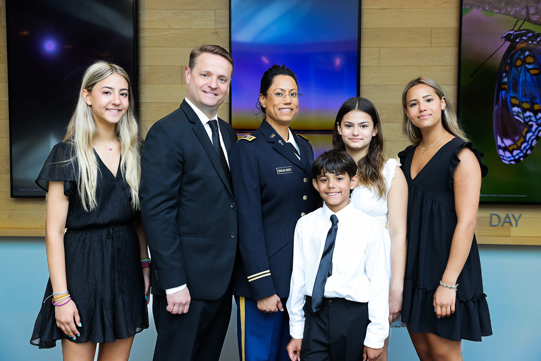 A smiling family photo comprised of (l to r) a teenaged girl, a man, a woman, a young boy, a slightly older girl, and another teenaged girl. 