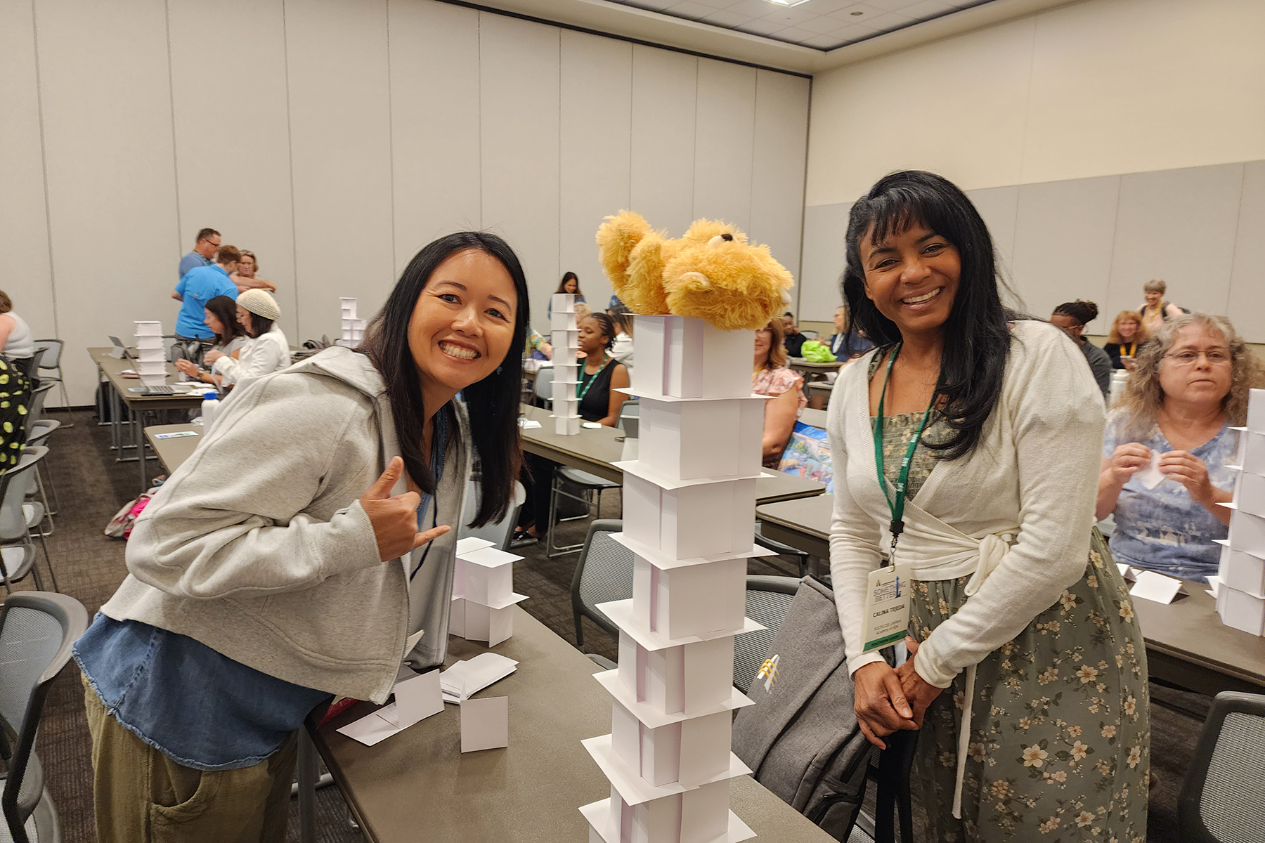 Two Asian women stand beside a tower built of postcards. 