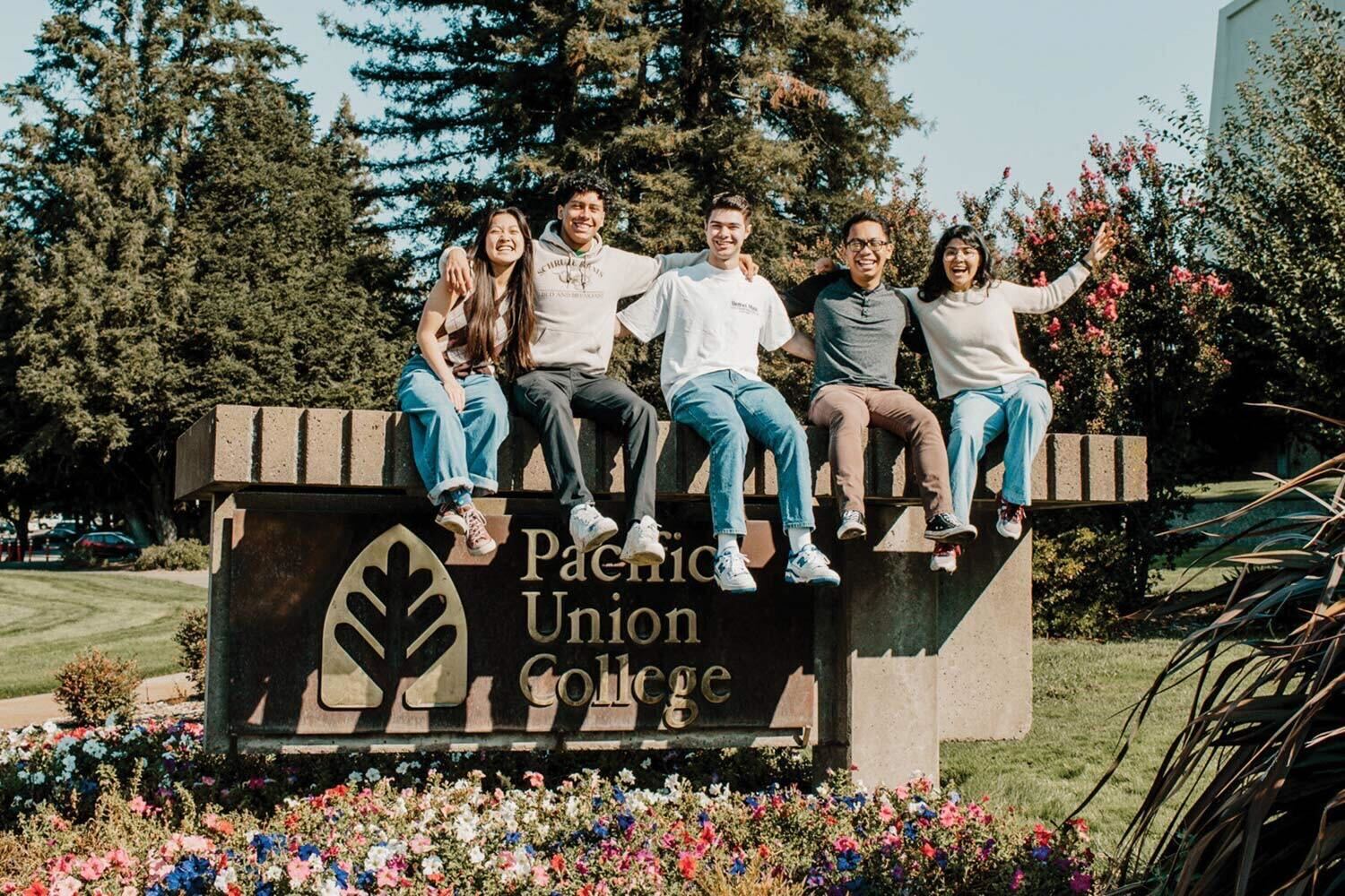 Picture of a small group of students sitting on a sign reading "Pacific Union College."
