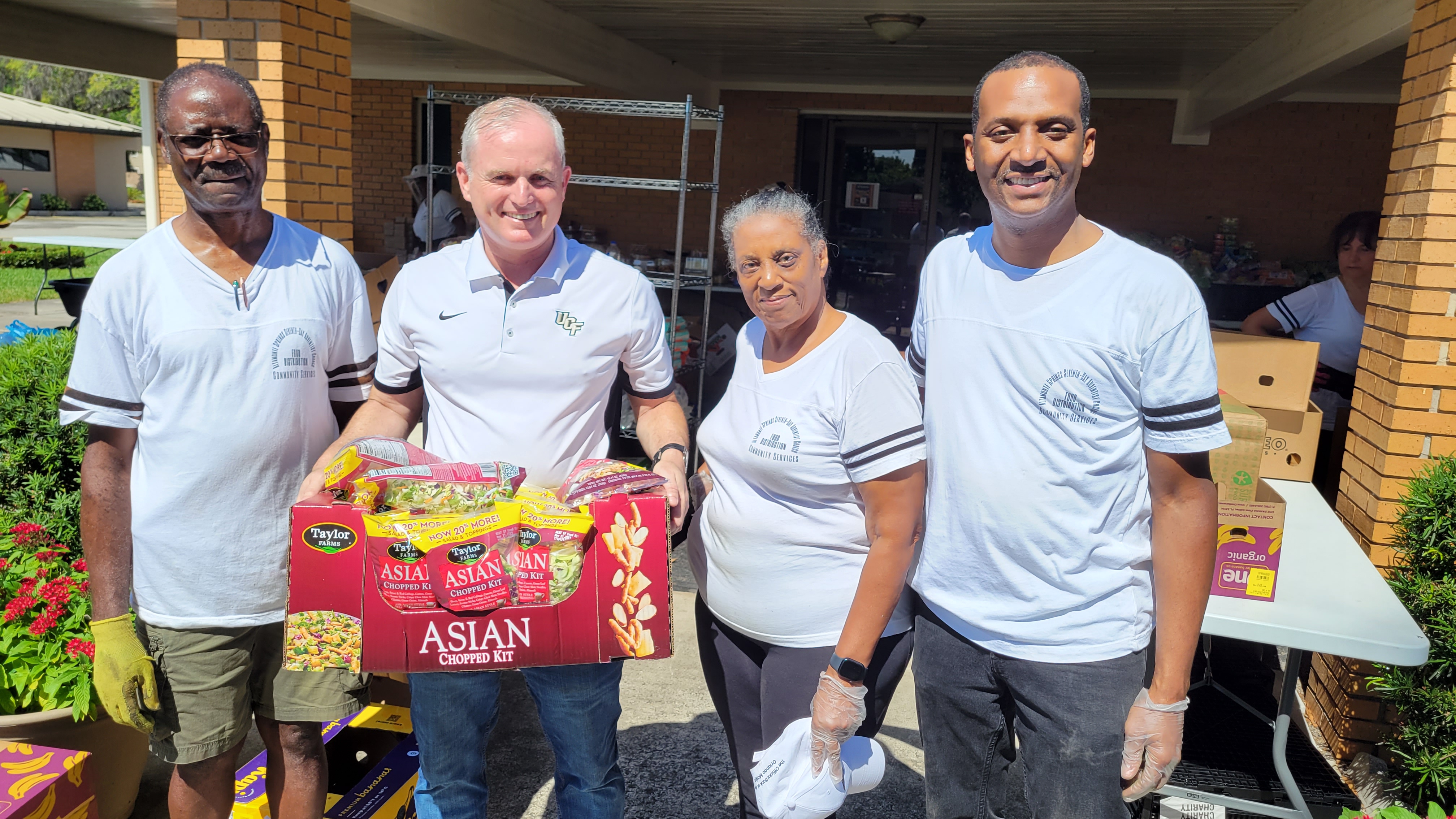 A group of people stand together smiling - black man, white man holding a box of Asian chopped kit, a black woman and black man
