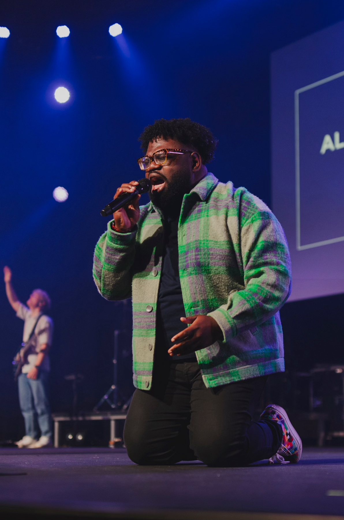 Black man on stage kneeling and singing into a mic.