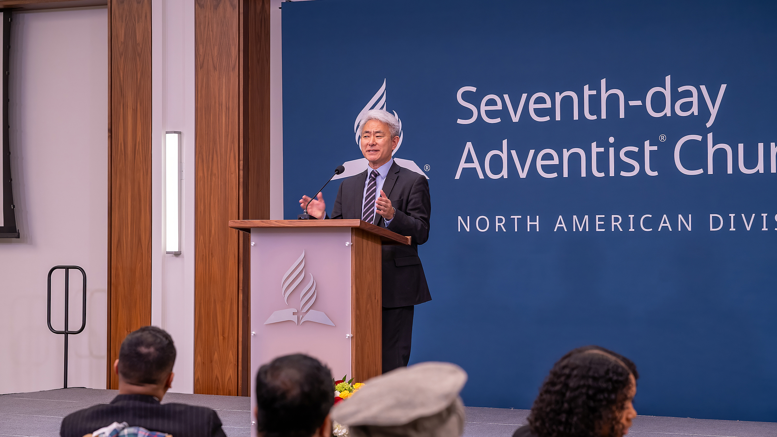 Asian man speaks behind a podium in front of a crowd