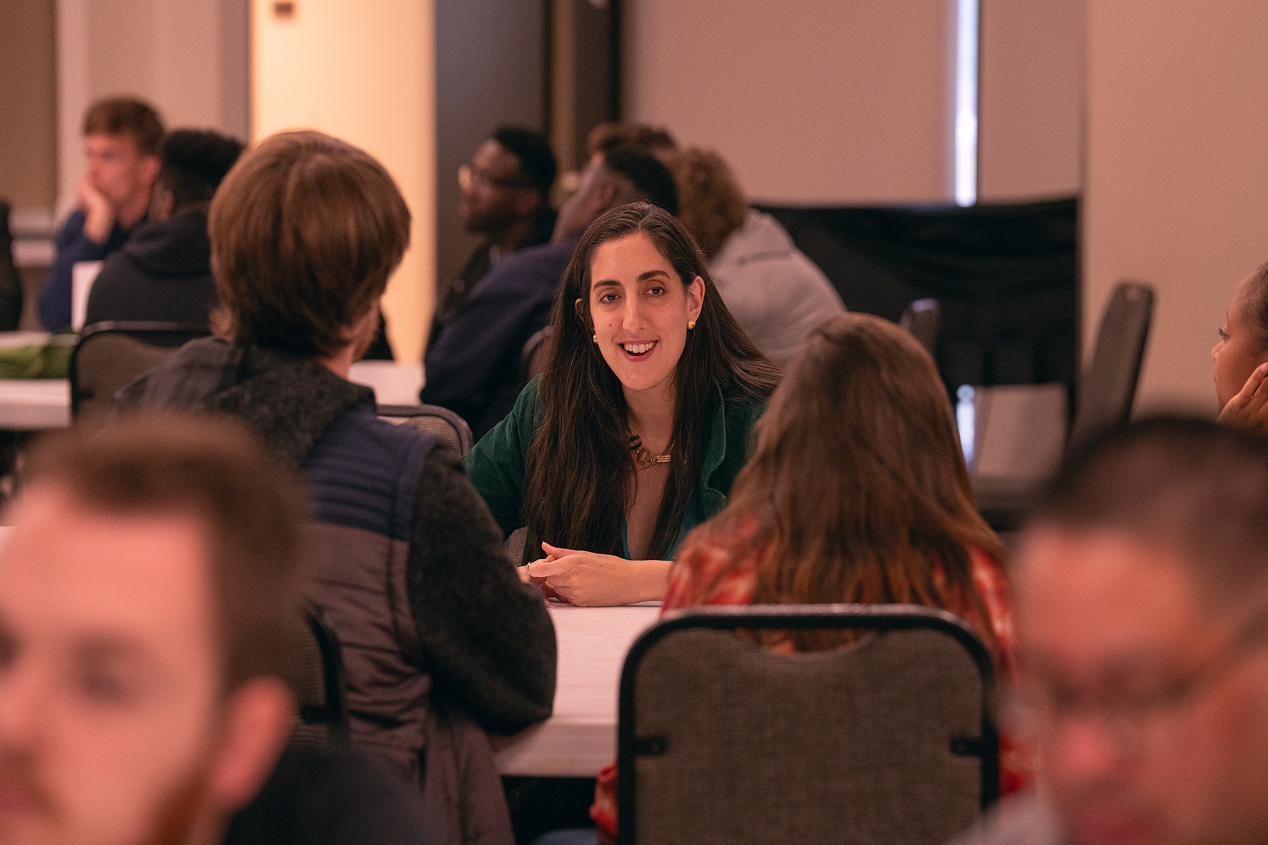 Photo of a white woman sitting at a table, surrounded by people of other ethnicities.