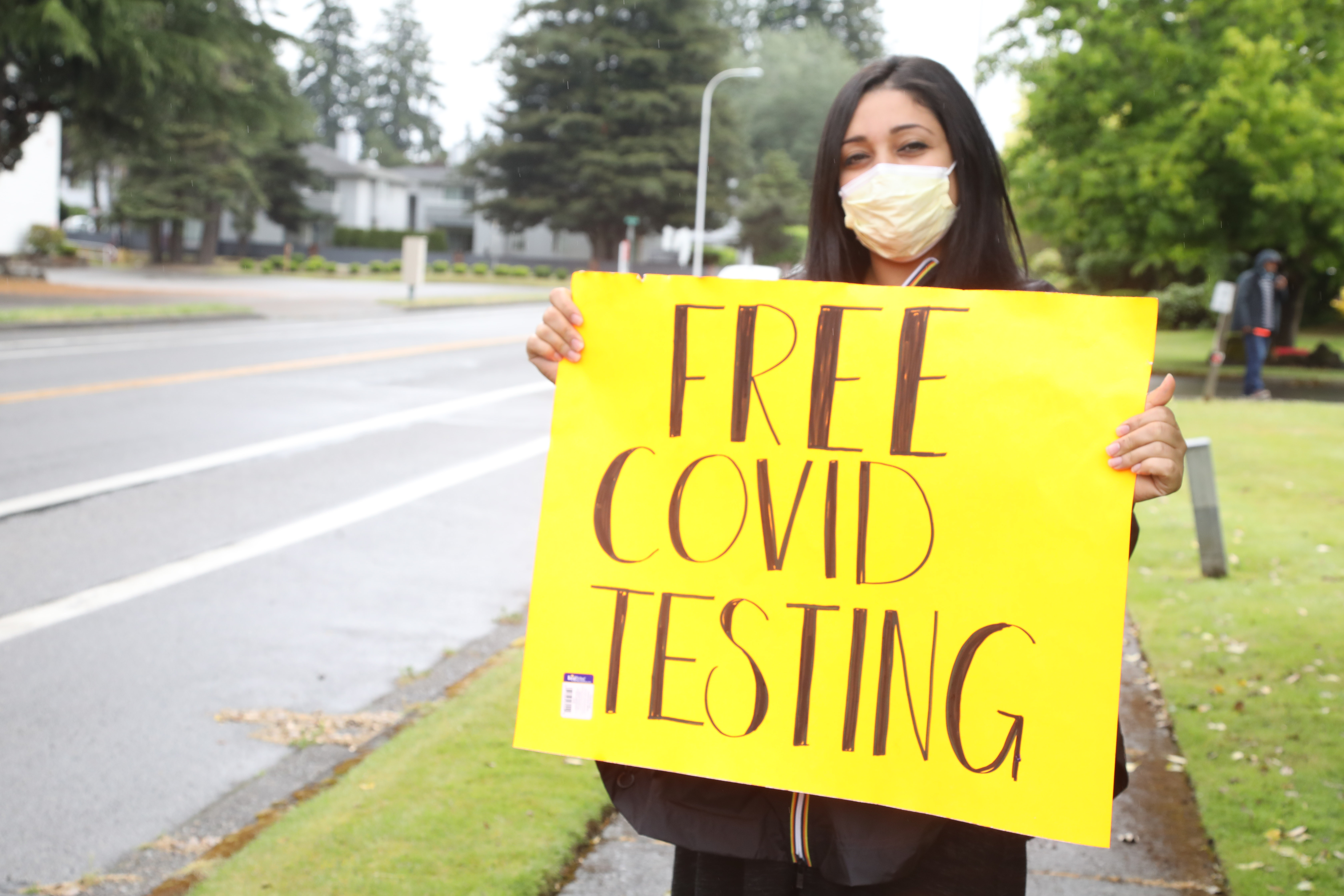 Jackie Langi holds a sign informing drivers about free COVID-19 testing and food boxes. 