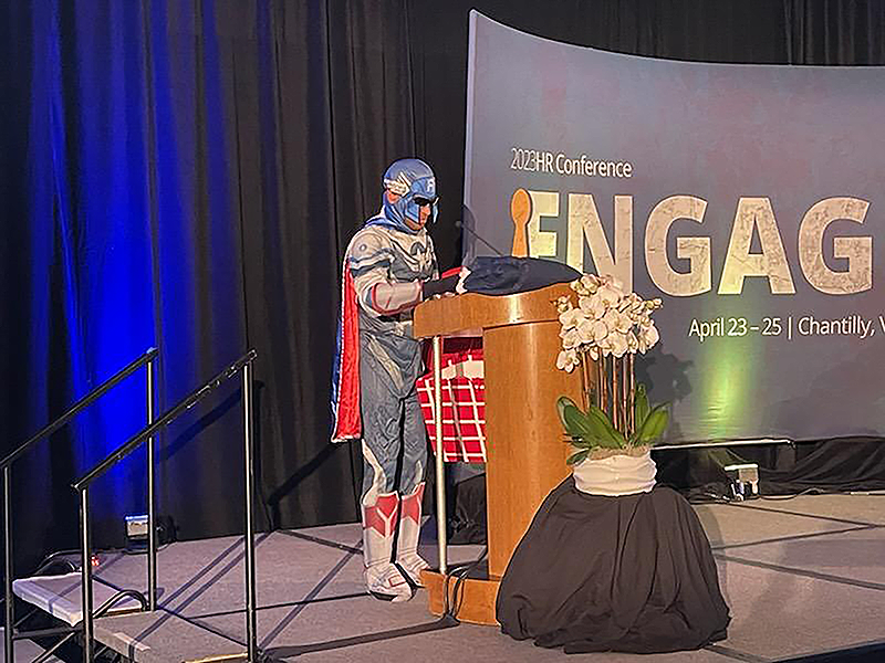 Man in superhero suit on 2023 HR Conference stage