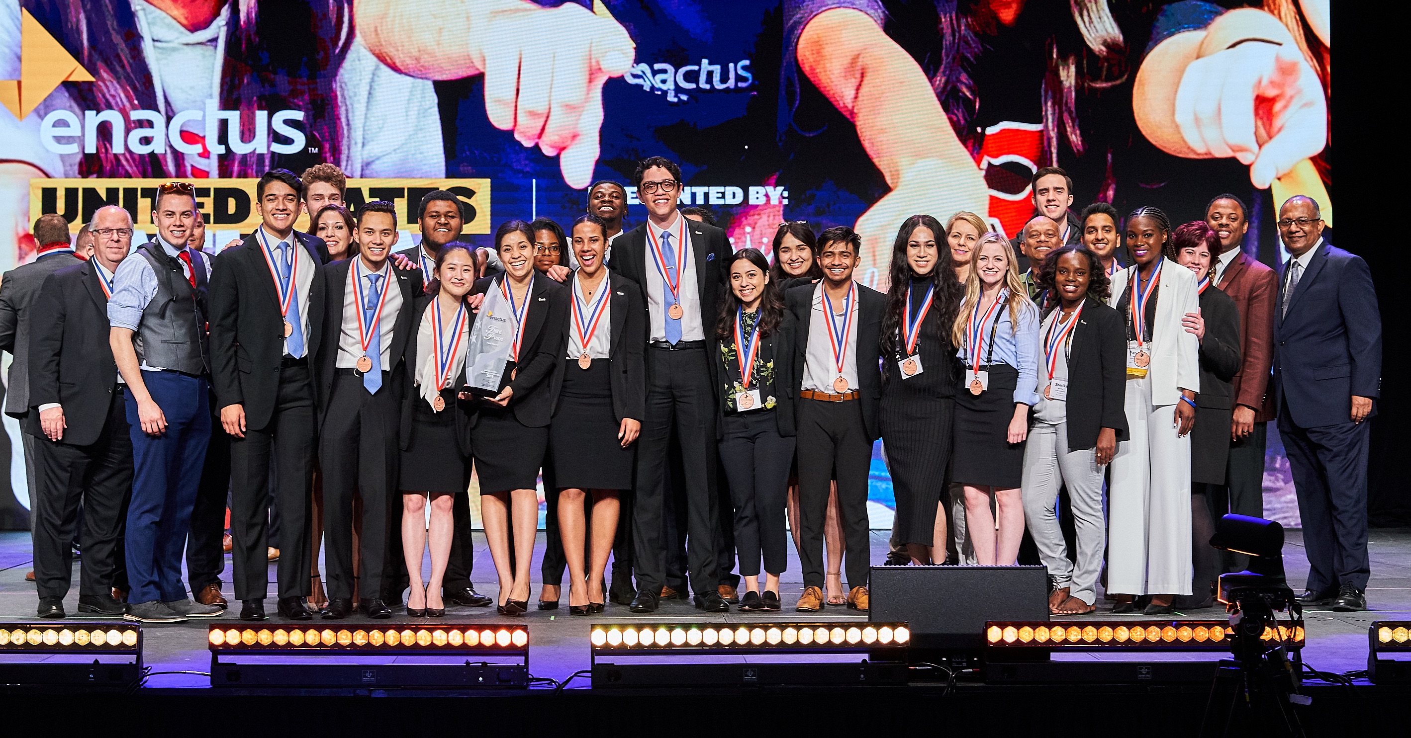 The La Sierra University Enactus team including national competition presenters and the eLibrary project team together on stage at the Enactus U.S. National Exposition, Kansas City Convention Center, Kansas City, Mo. with team members' parents, Zapara School of Business Dean John Thomas, far right, and business school Professor Jere Fox, far left.