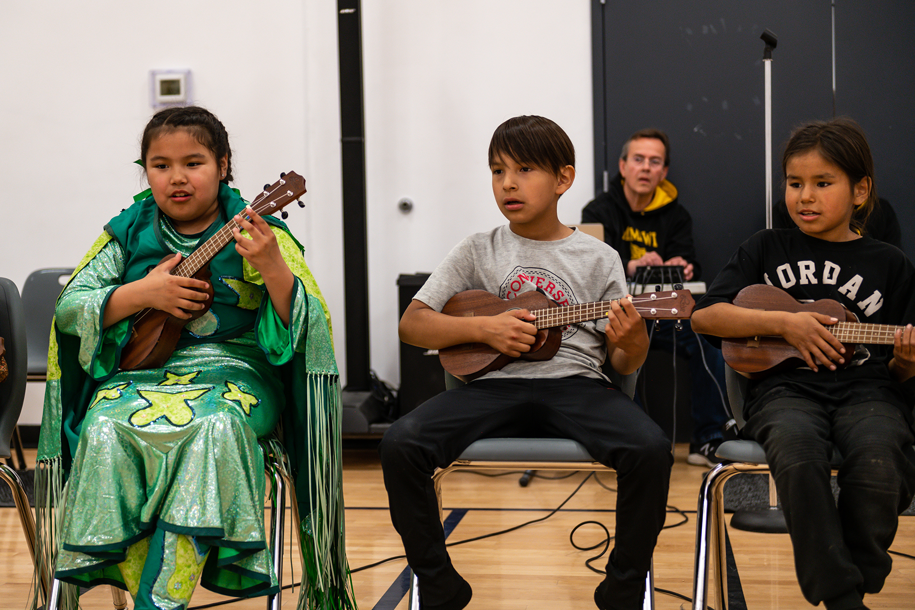 Three young Indigenous children seated in a row playing the ukelele