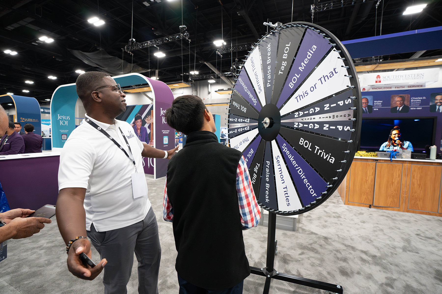 An exhibitor interacts with a guest spinning a wheel for prizes.