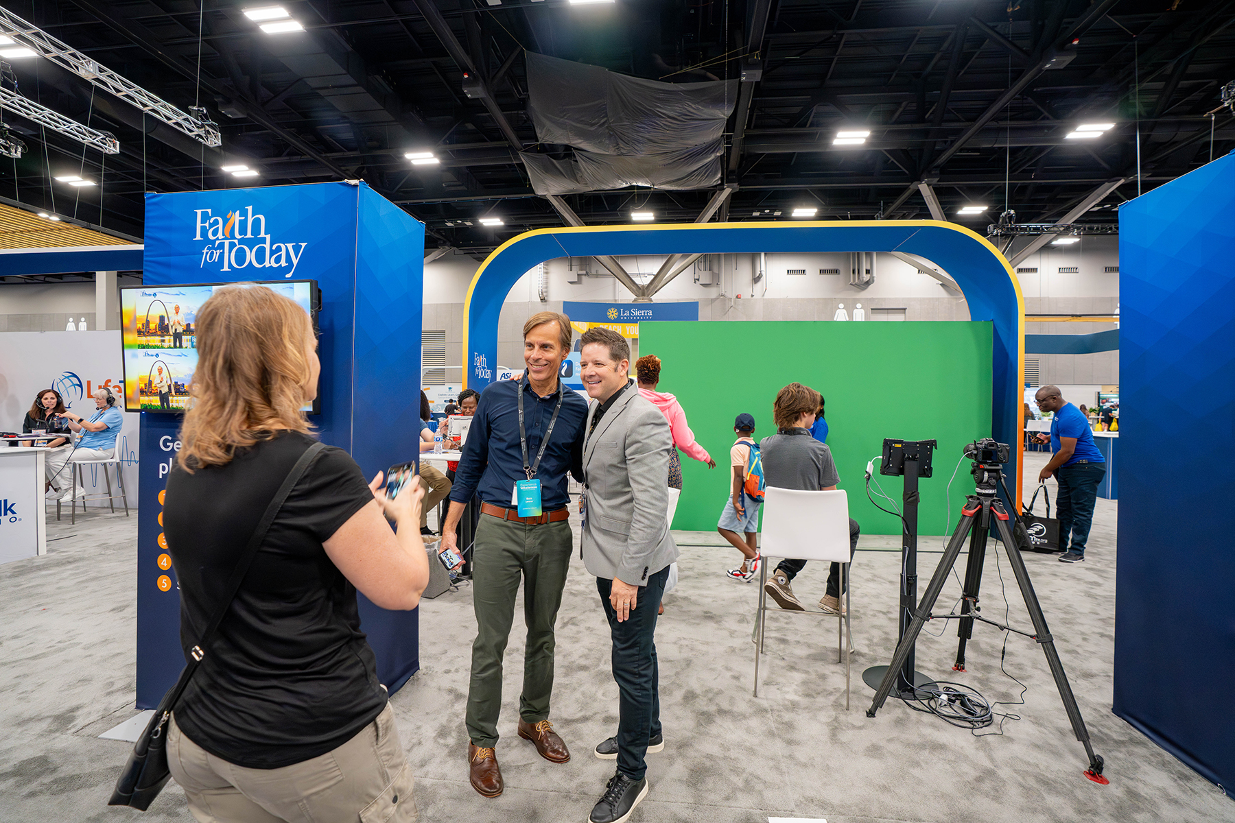 Men pose in front of the Faith for Today exhibit while visitors interact with a green screen.