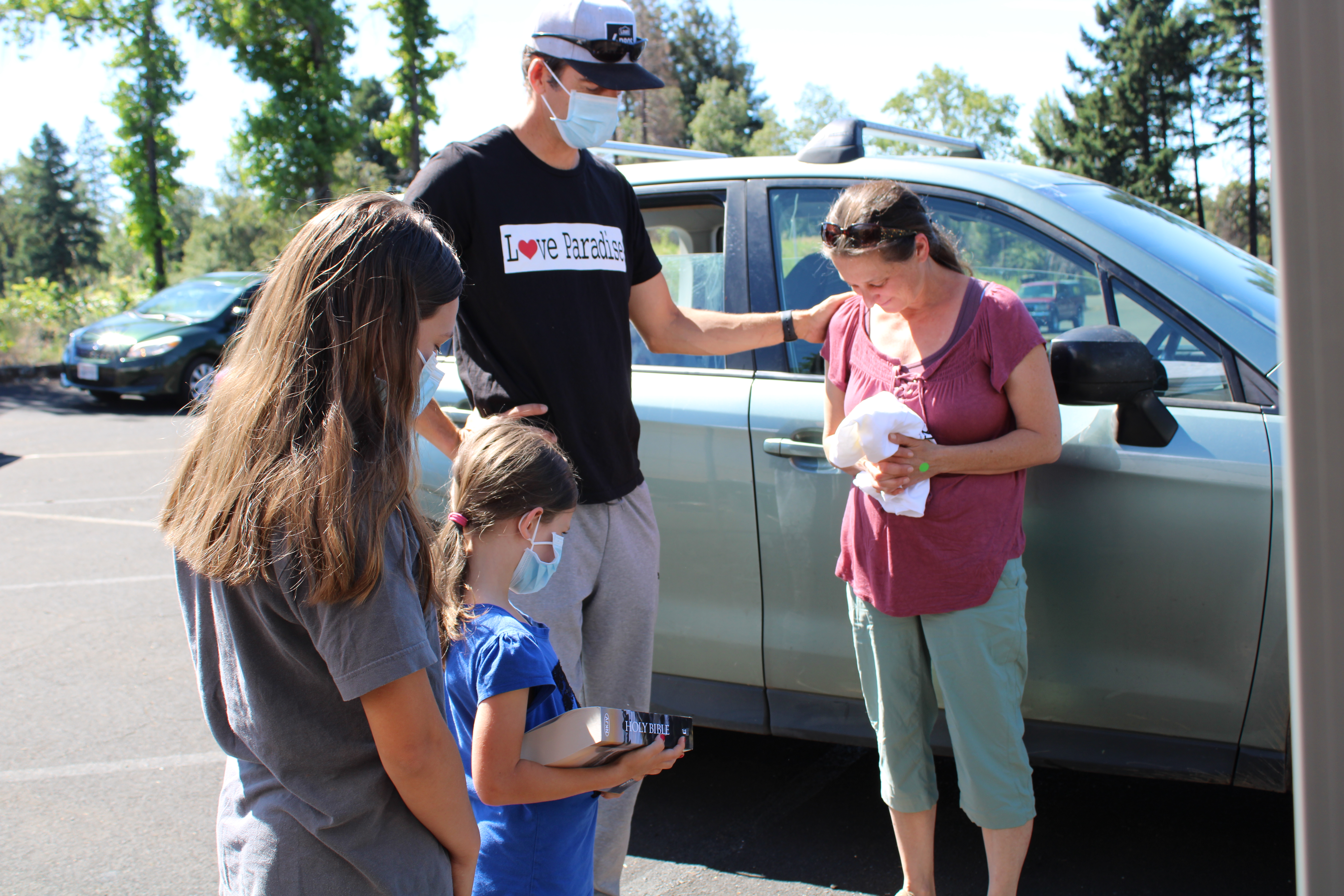 Pastor Garrison Chaffee prays with a grateful recipient of fresh food with Kyla and Rachel Moore. The food pick up was at the Paradise church parking lot. The church burned but serving others is still their priority.   