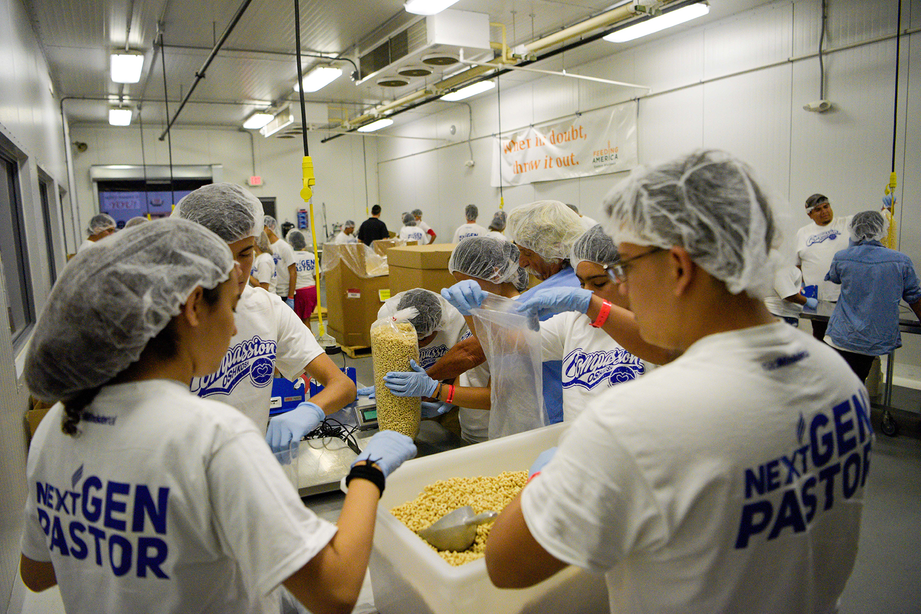 young people wearing hair nets packing cereal into plastic bags. 