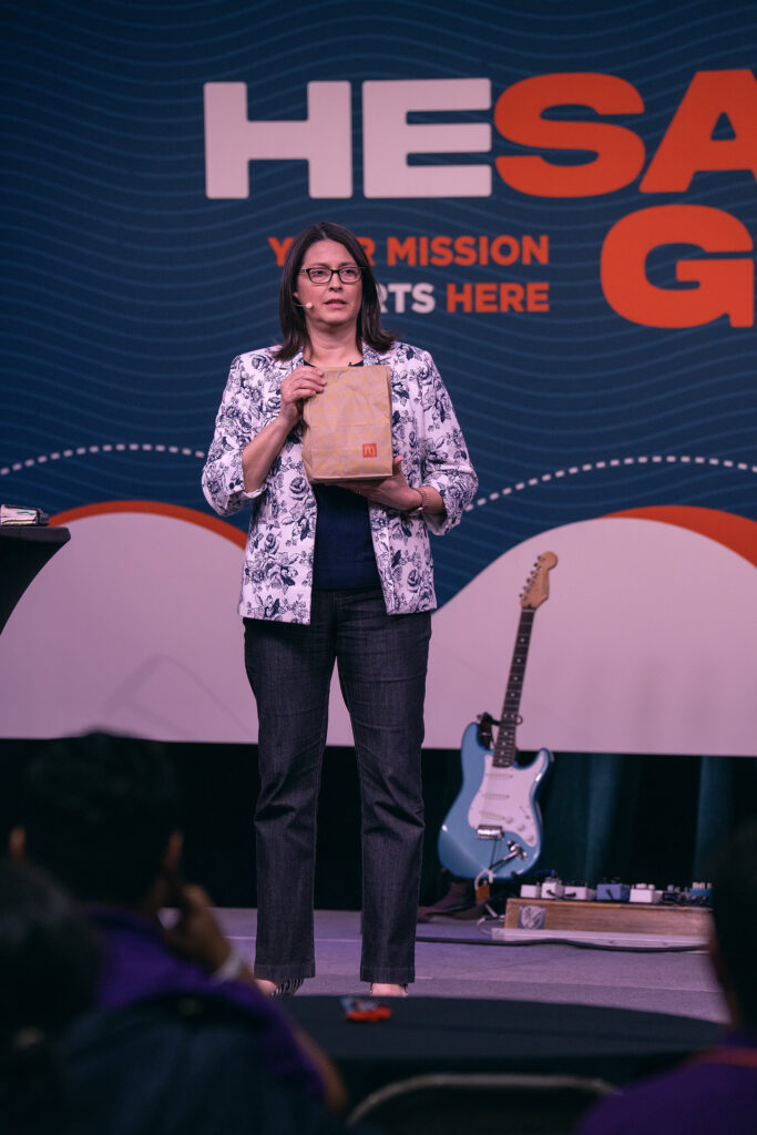 Woman stands on HeSaidGo XP stage holding a McDonald's bag