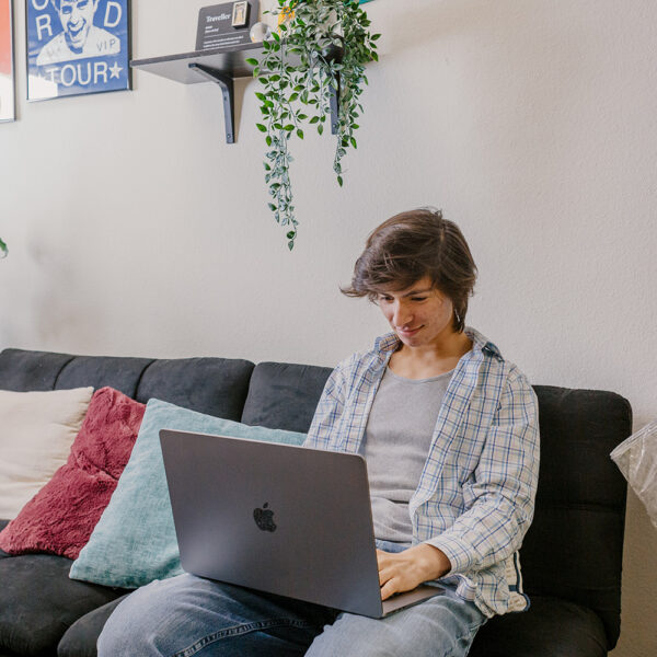 Caucasian male college student sits on sofa with Mac laptop computer.