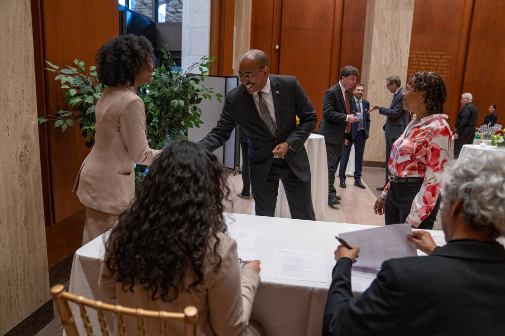Guests greet each other near a reception table in a conference room. 
